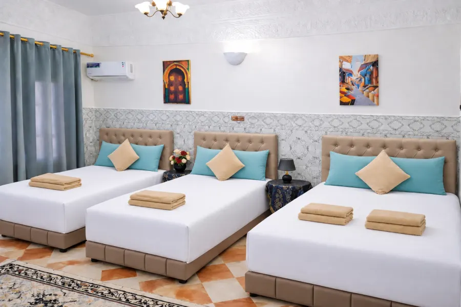 Bright room with three beds, turquoise cushions and a patterned tiled floor